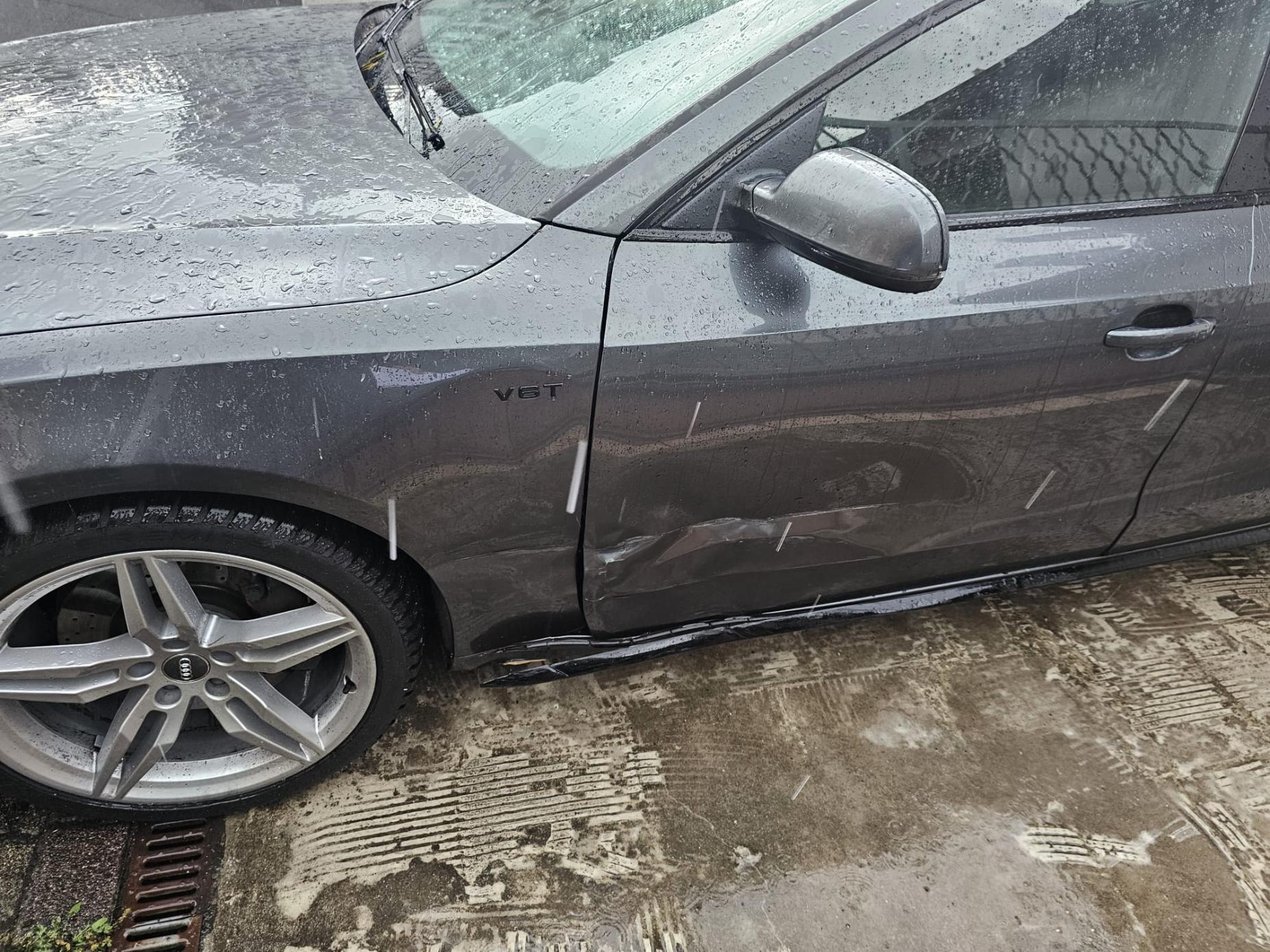 Seitenschaden grau: Lange Schramme und Delle an der Fahrerseite eines grauen Autos.